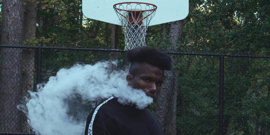 a black man smoking outdoors at a basketball court