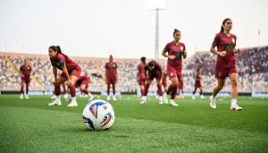 Women’s football players warming up on a stadium pitch in Morocco with the crowd and stadium stands blurred in the background.